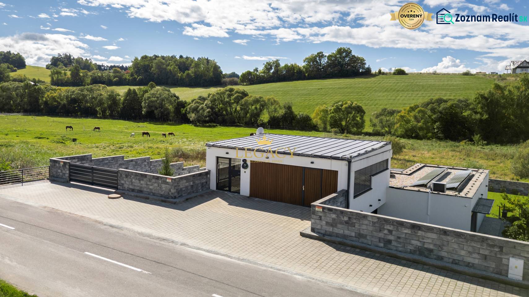 A family house in Dolný Kalník surrounded by green meadows and horses, with a stone fence.