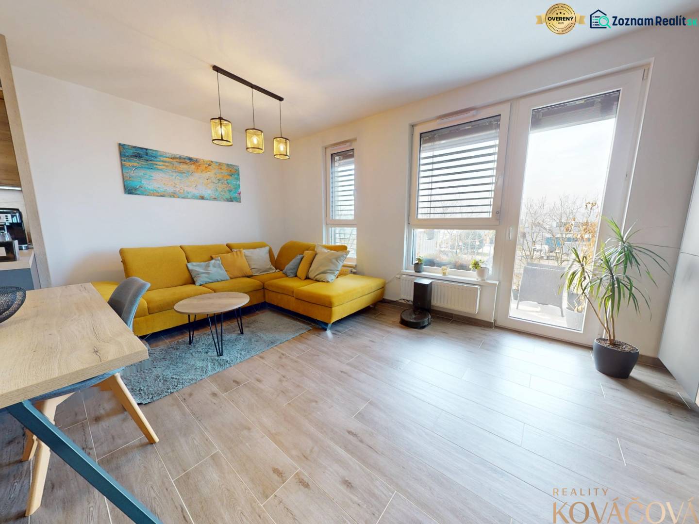 Living room of a three-room apartment with a wooden decor floor, a yellow sofa, and a large window.