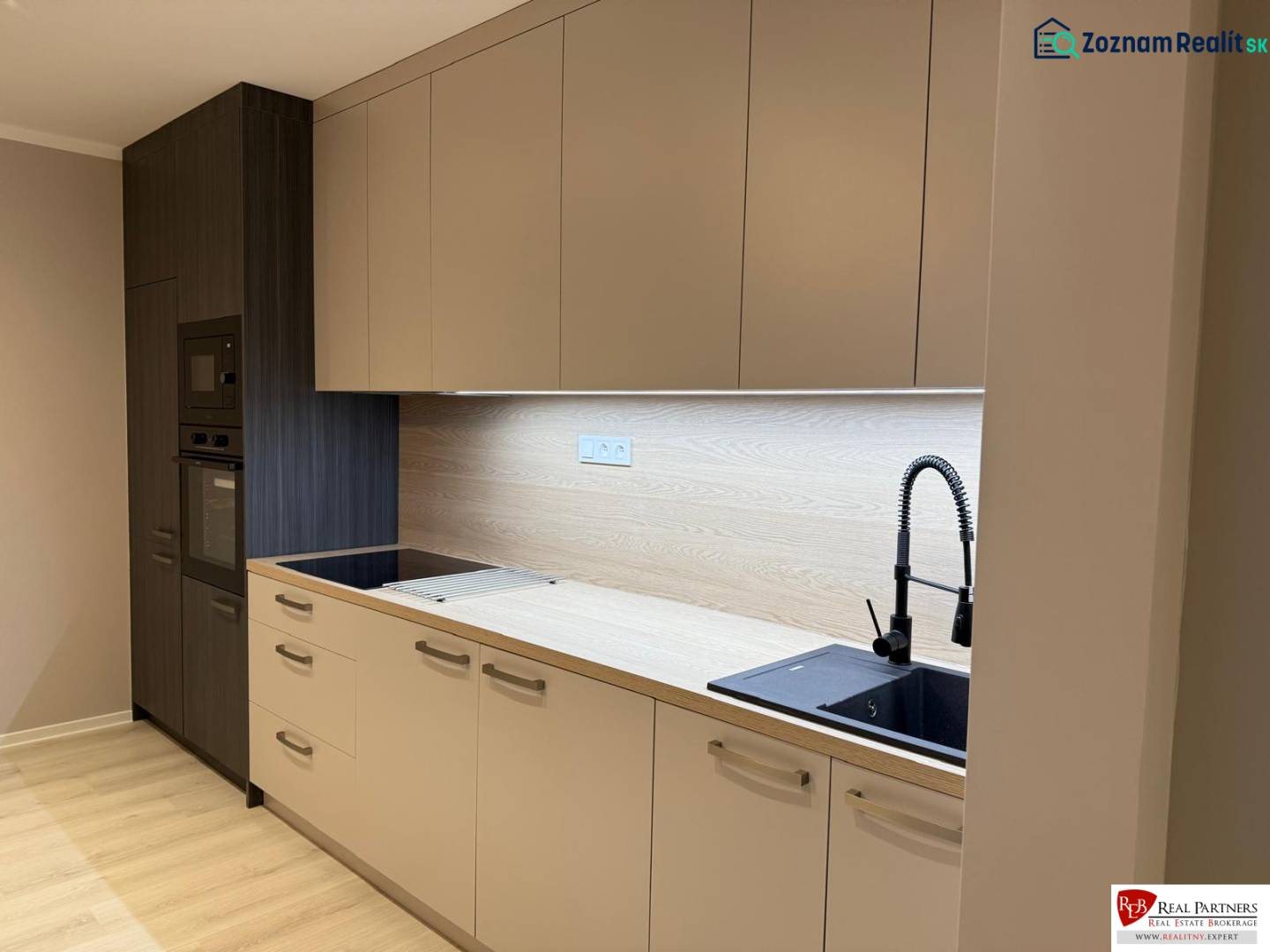 A kitchen unit in a 2-room apartment with a wooden decor floor and built-in appliances.