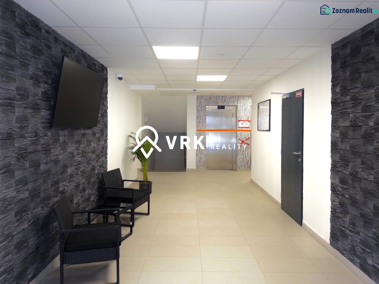 Hallway in a 3-room apartment with a TV on the wall and an elevator in the background.