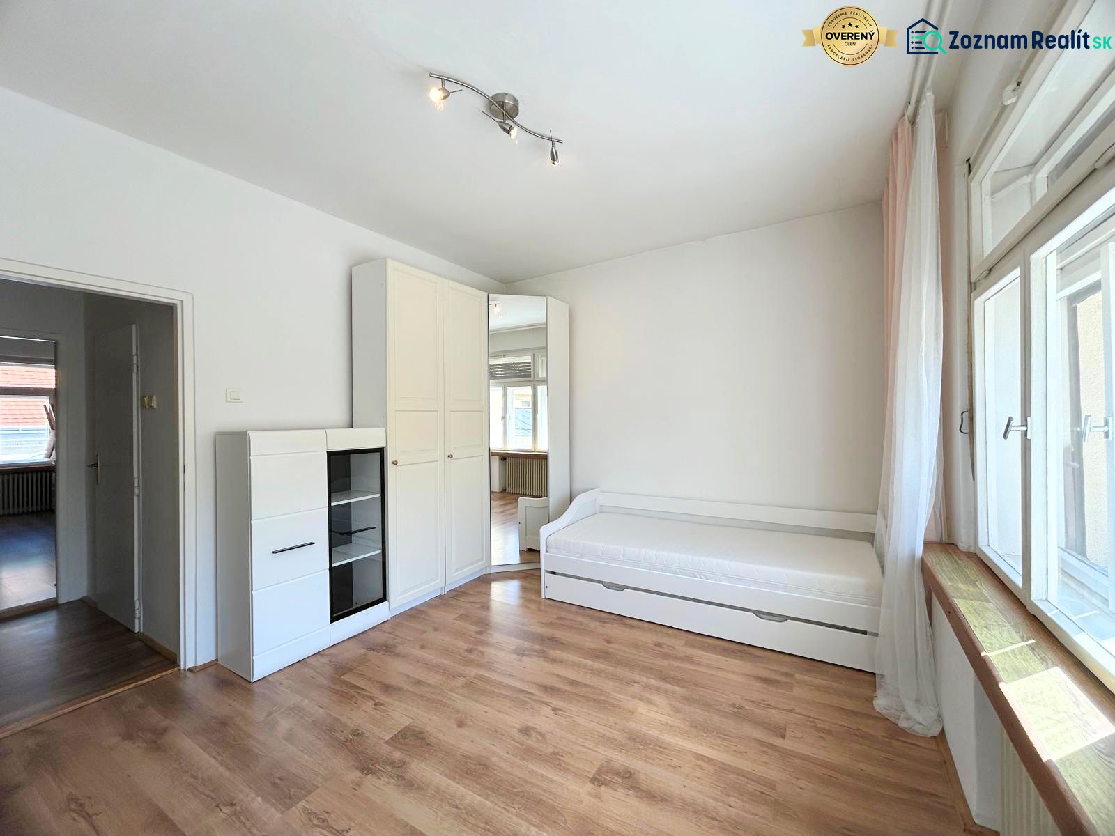A bright room space in a 2-room apartment with a bed, a cabinet, and a large window.