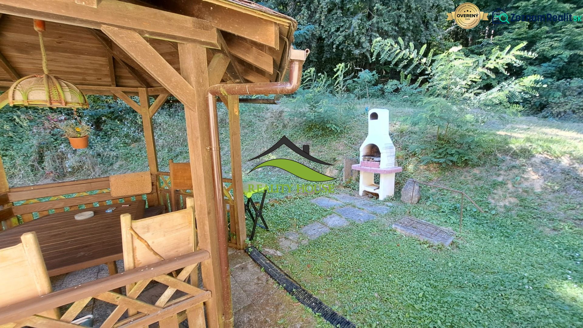 A wooden gazebo with a grill at the cottage in Dobrá, Kvakovce, surrounded by greenery and trees.