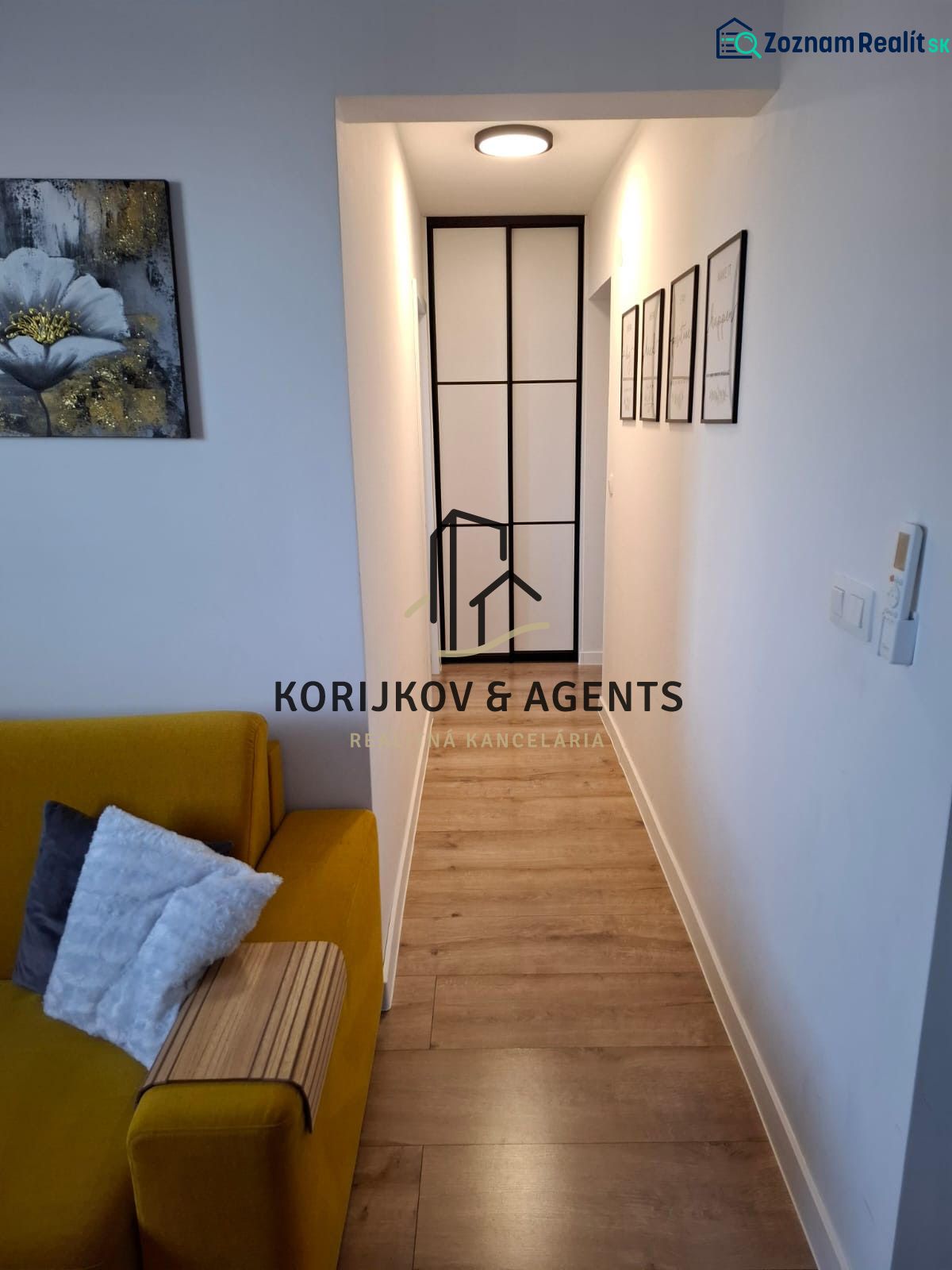 A narrow hallway in a 2-room apartment with a wooden-patterned floor and a yellow sofa.