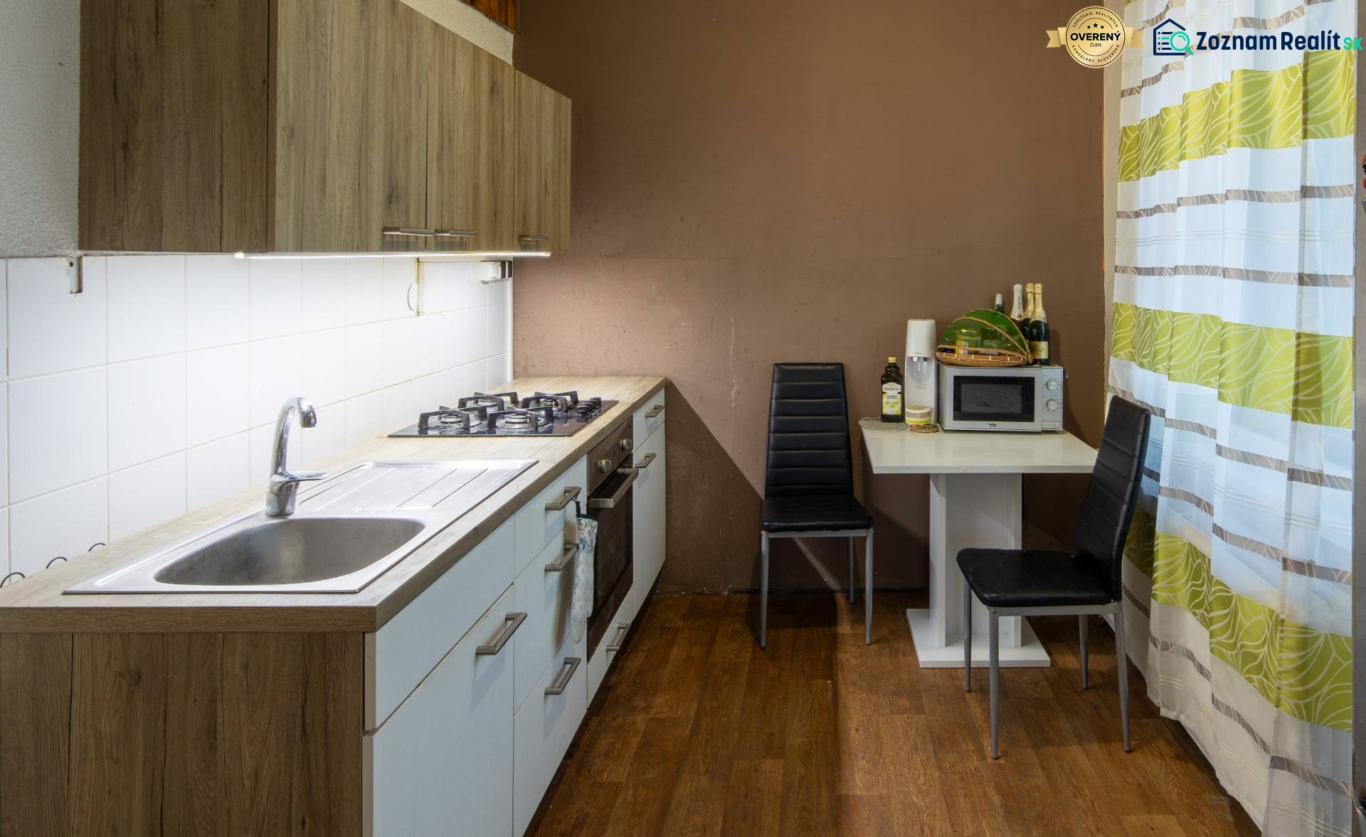 The kitchen of a two-room apartment with a wooden-patterned floor and a dining area.