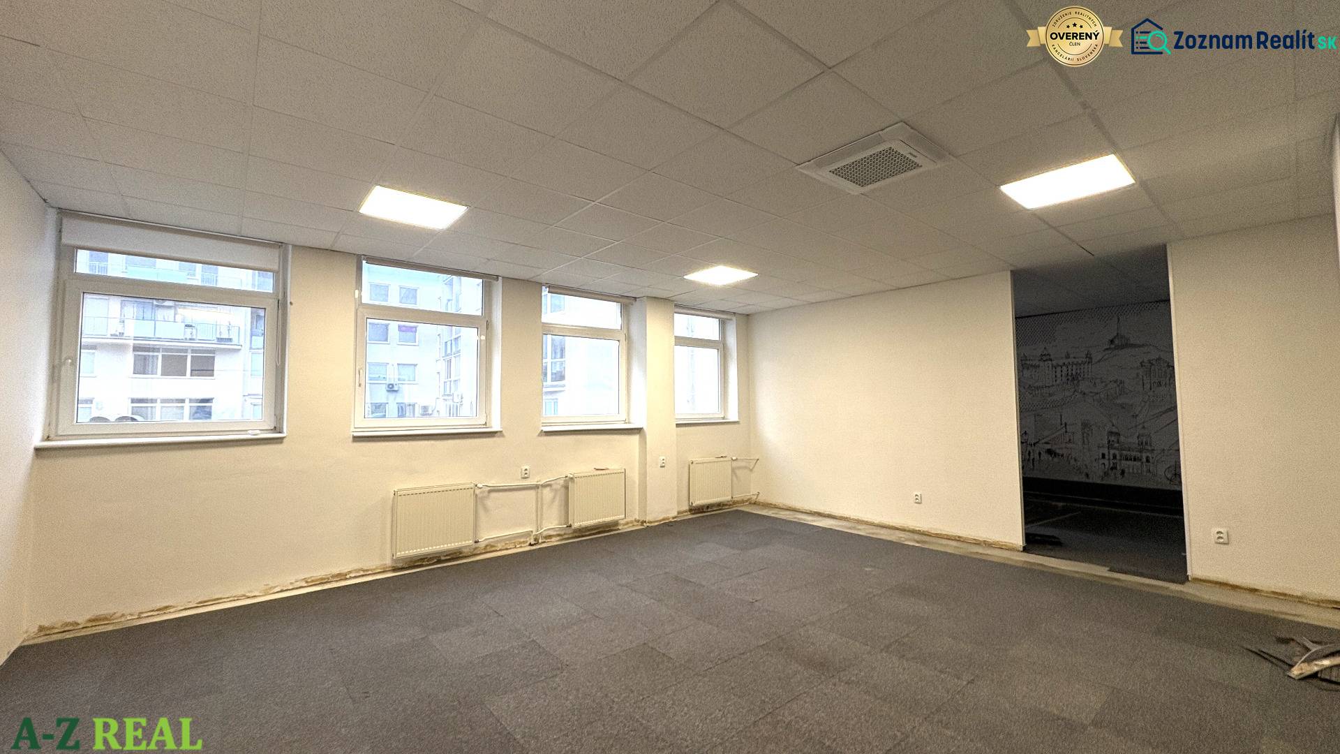 Carpeted offices, large windows, white walls, ceiling lighting.
