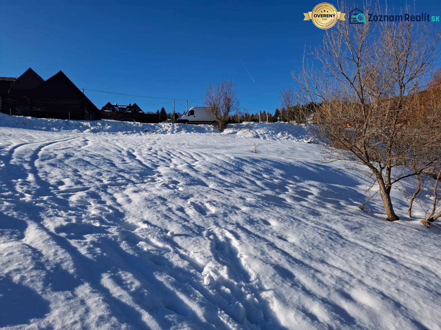 Snow-covered residential lands in Ždiar with trees and a blue sky.
