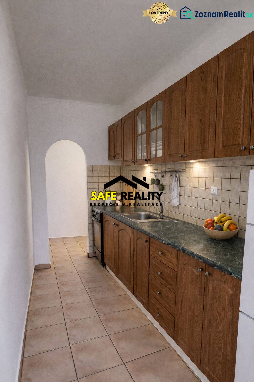A narrow kitchen in a 2-room apartment with wooden cabinet decor and an arched doorway.