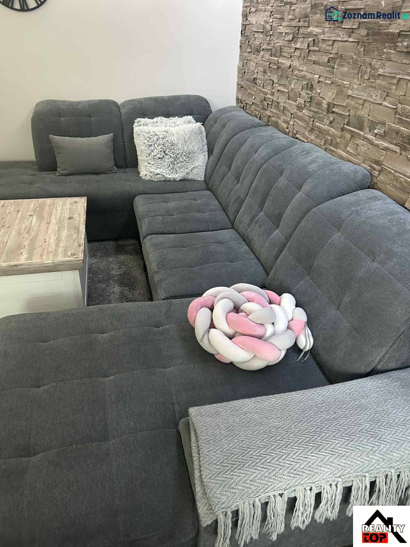 Gray sofa with cushions by a stone wall in a 3-room apartment.