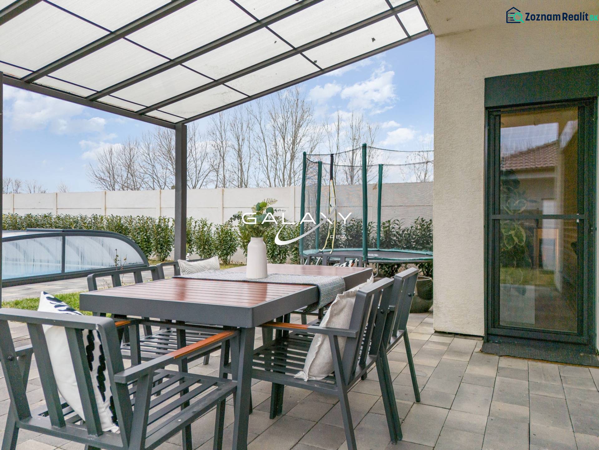 Terrace of a family house in Dunajský Klátov with a seating area, covered swimming pool, and trampoline.