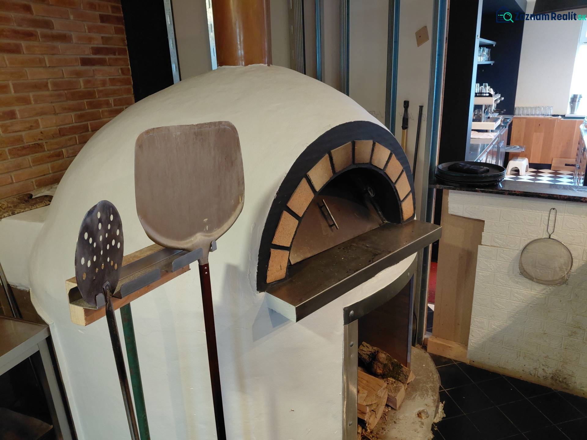 Pizza oven and tools in a gastro space with firewood and a brick wall.
