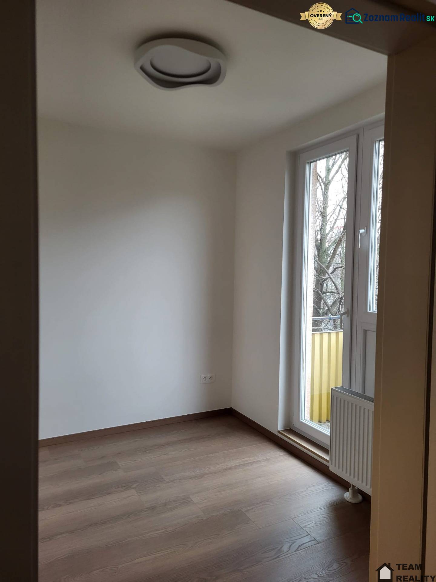 A room in a 2-bedroom apartment, floor with wood decor, large window to the balcony.