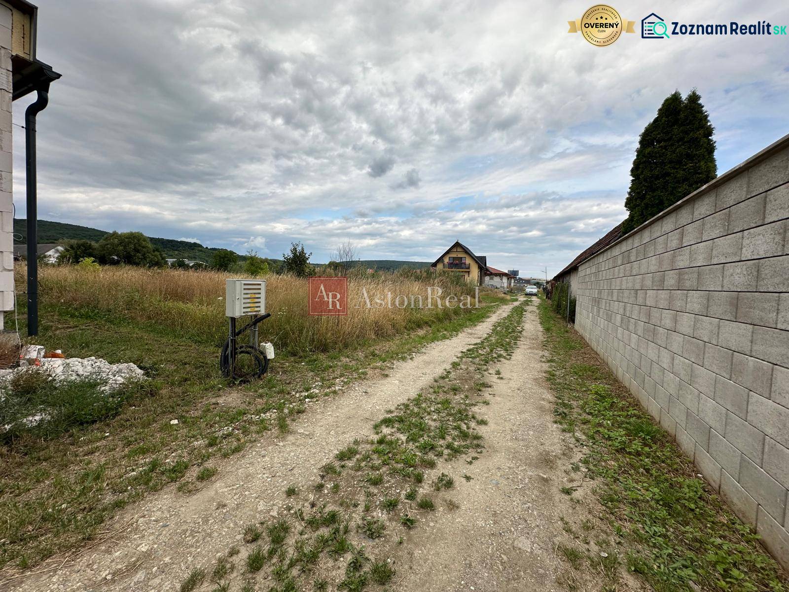 A dirt road surrounded by grassy residential plots on Poľnohospodárska Street in Trenčín.