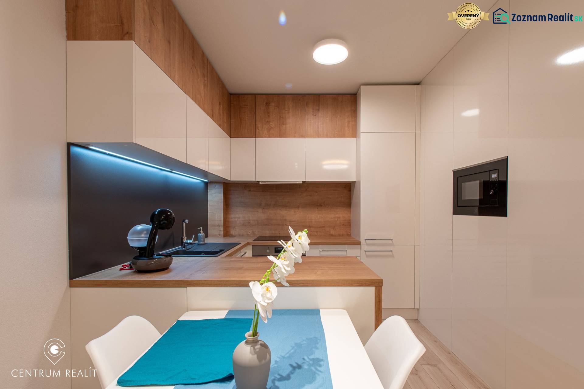 A kitchen in a 2-room apartment with light furniture and a wooden decor floor.