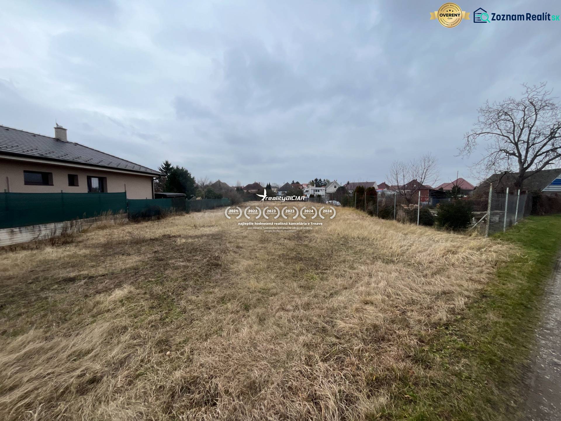 Building plot for housing in Hlohovec, grassy area between houses under a cloudy sky.
