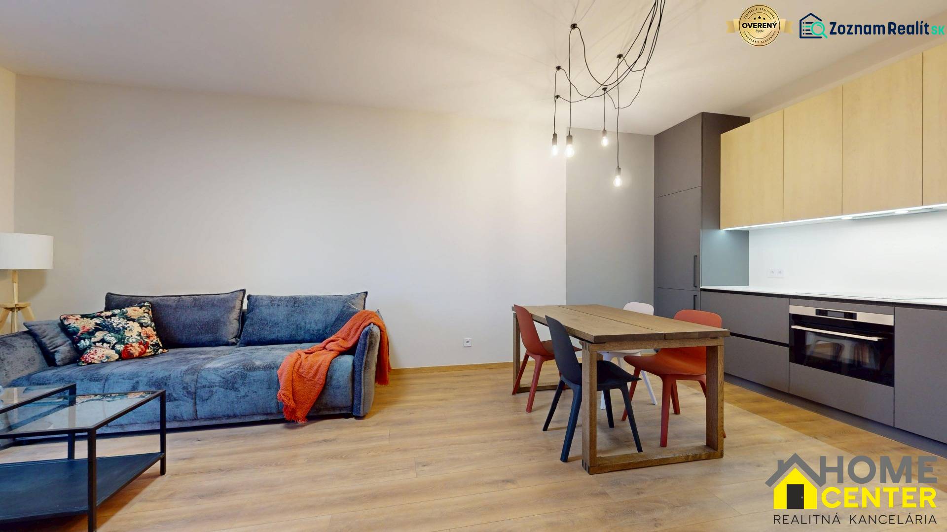 Living room in a two-room apartment with a sofa, dining table, and wooden decor flooring.