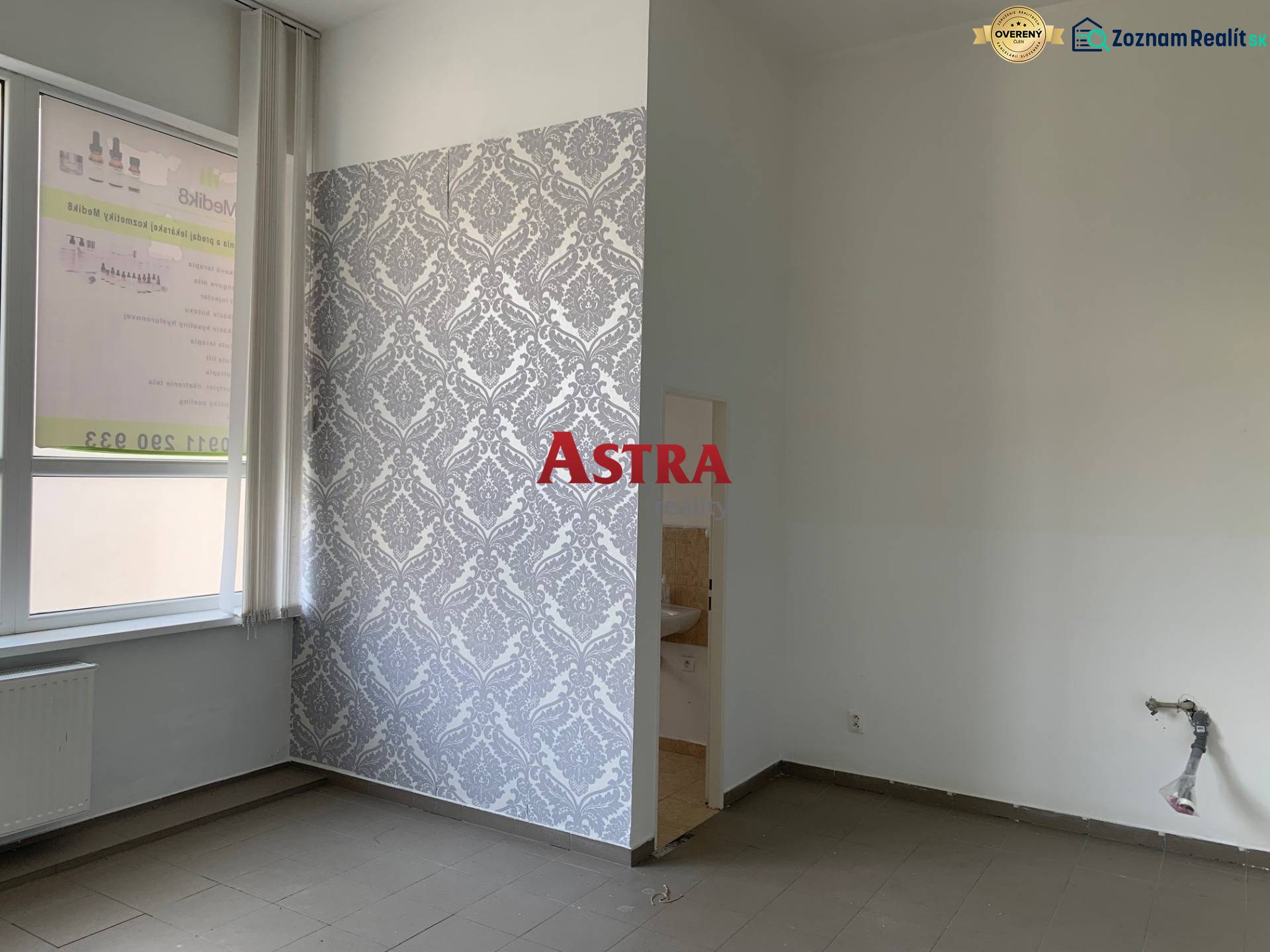 Interior of an office with a window, radiator, and tiled floor, patterned wallpaper on the wall.