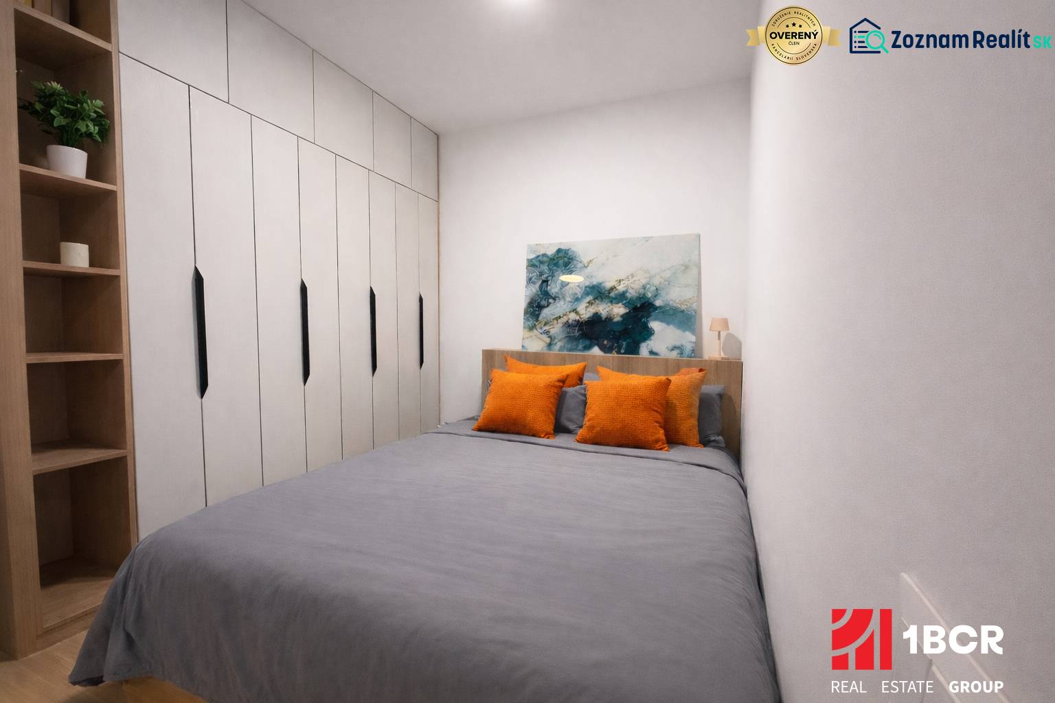 A bedroom in a studio apartment with a wardrobe, art on the wall, and orange pillows.