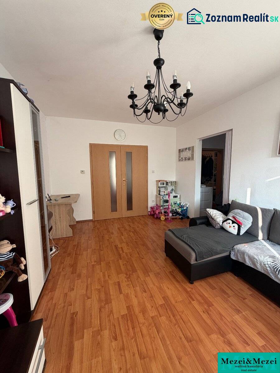 A room with a wooden decor floor, a sofa, a chandelier, and a door in a 2-room apartment.