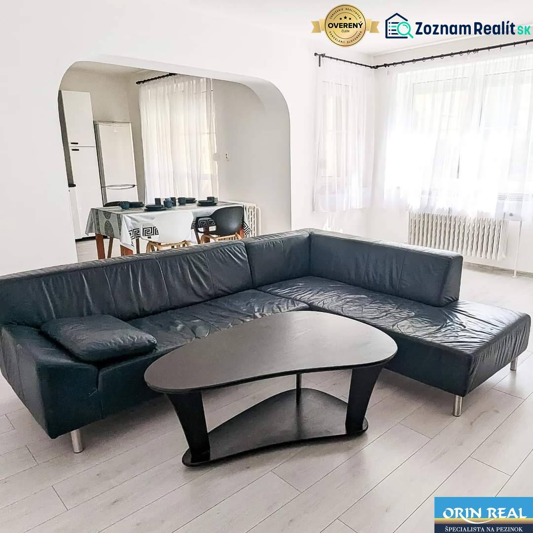 Living room in a two-room apartment with a leather sofa, a table, and a wooden decor floor.