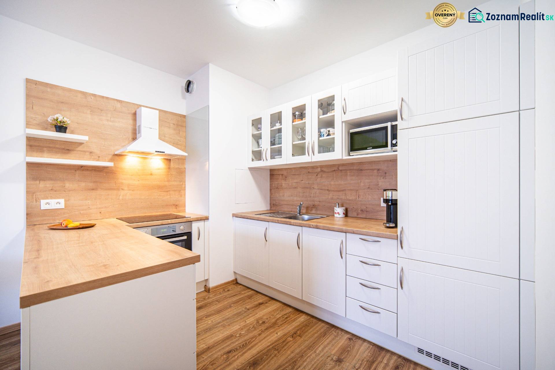 A bright kitchen with white cabinets and a wood-patterned floor in a two-room apartment.