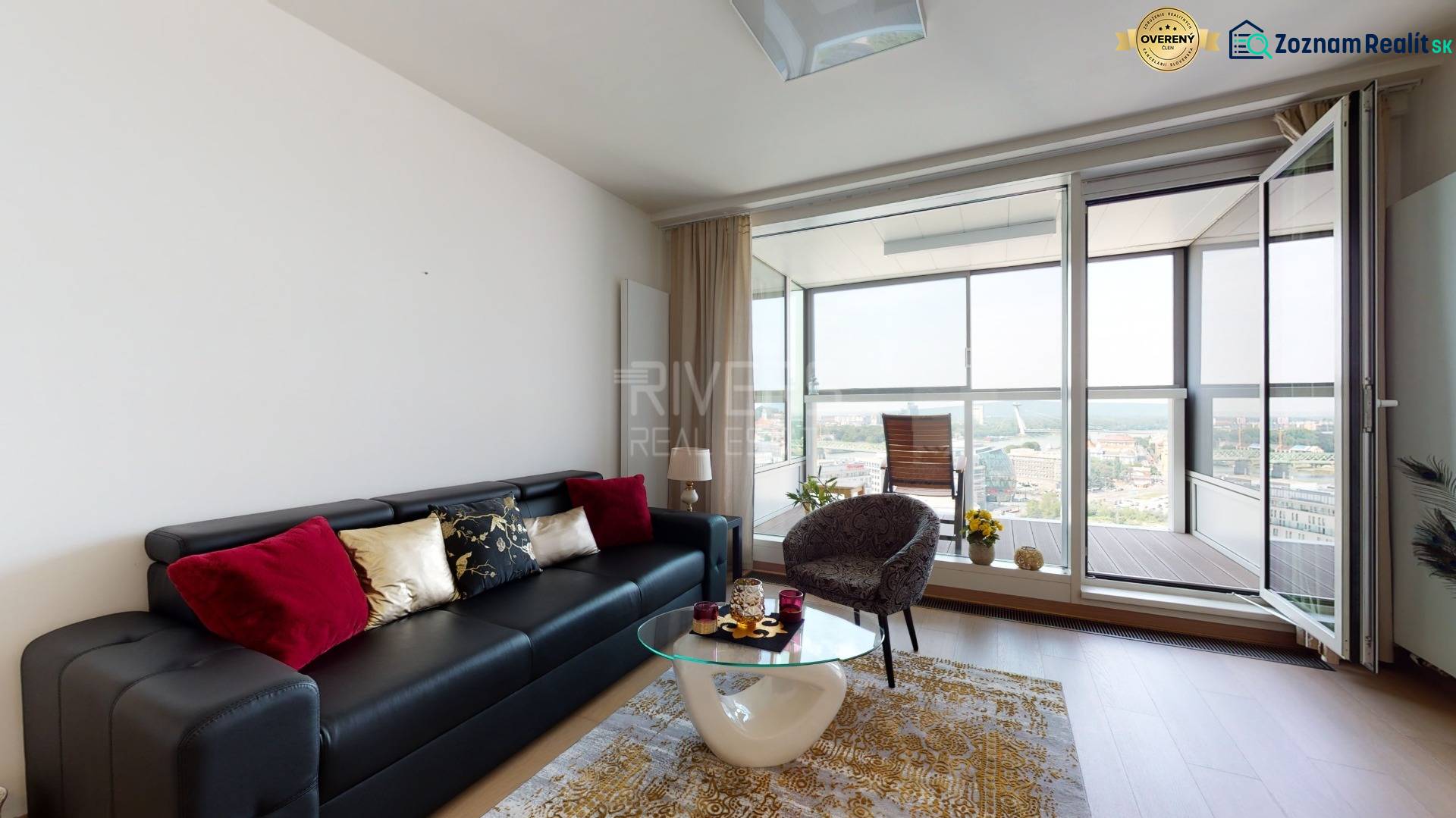 Living room of a three-room apartment with a sofa, armchair, and glass table, leading to a balcony.