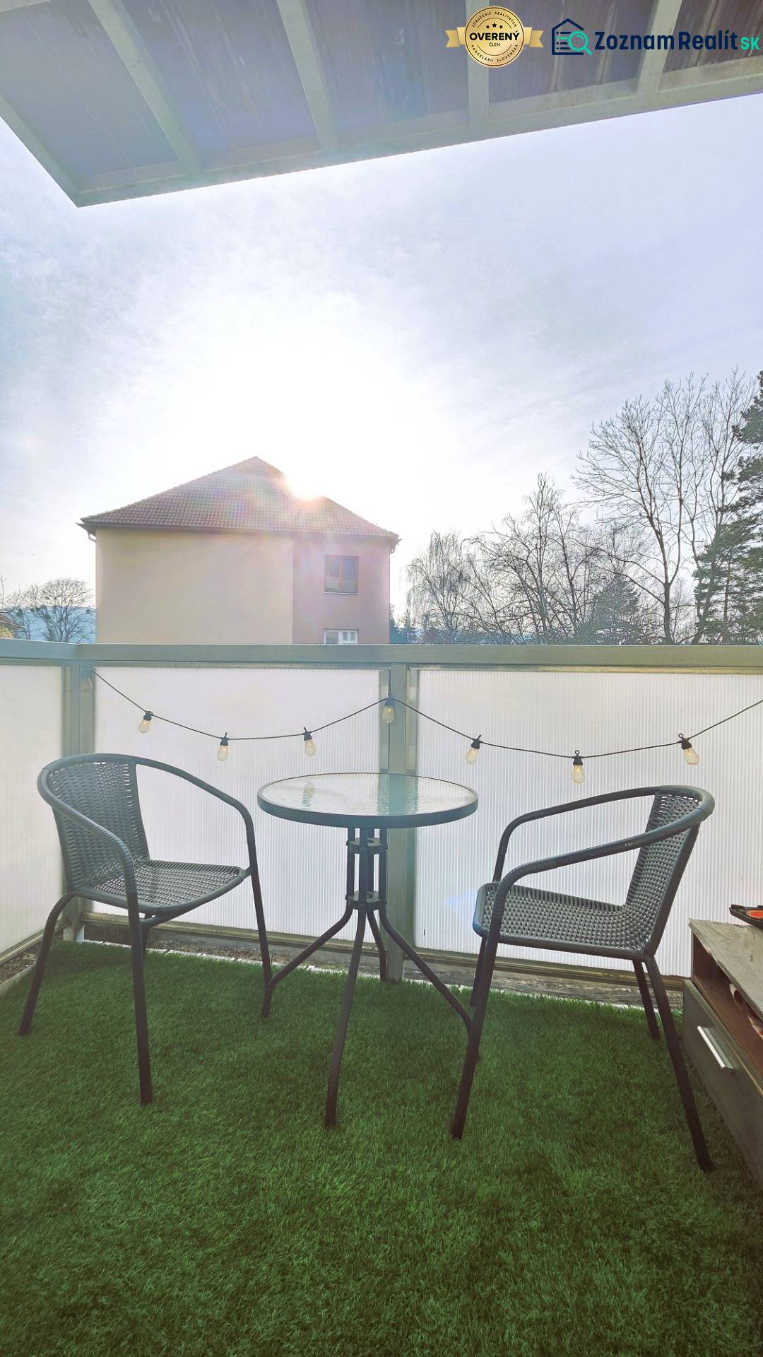 A balcony with two chairs and a table, with green grass on the floor.