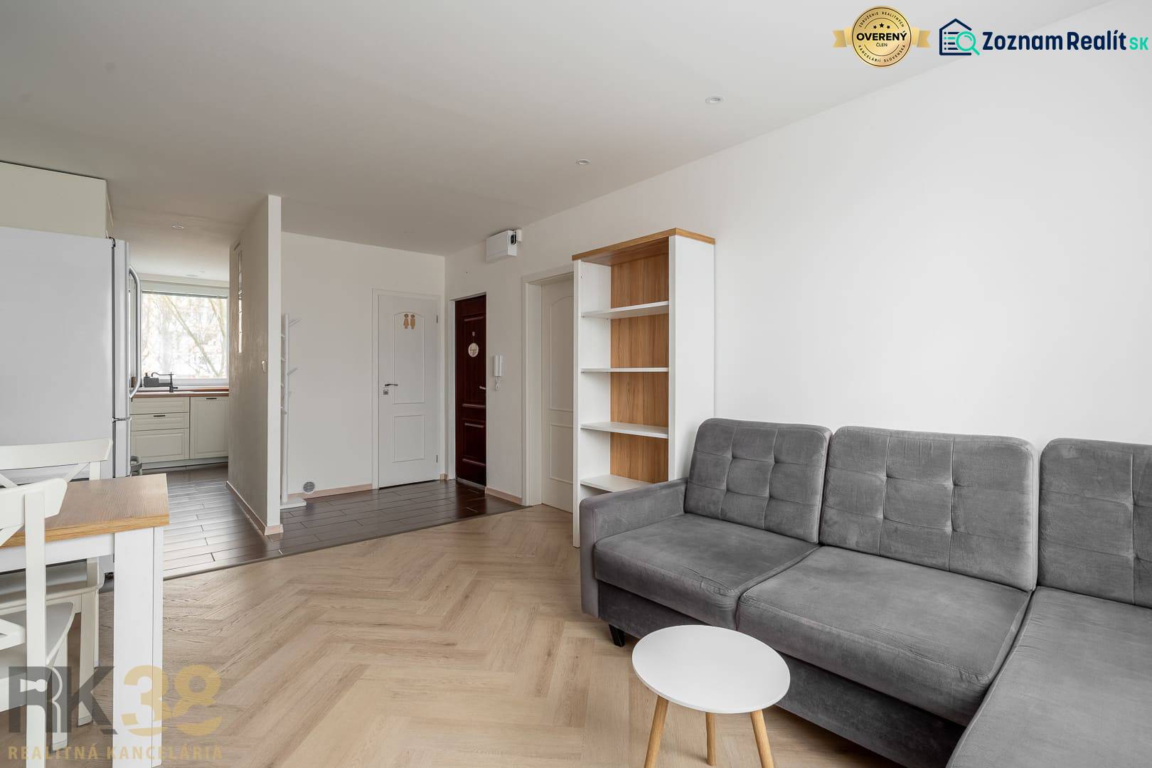 Living room in a three-room apartment with a wood-patterned floor and a gray sofa.