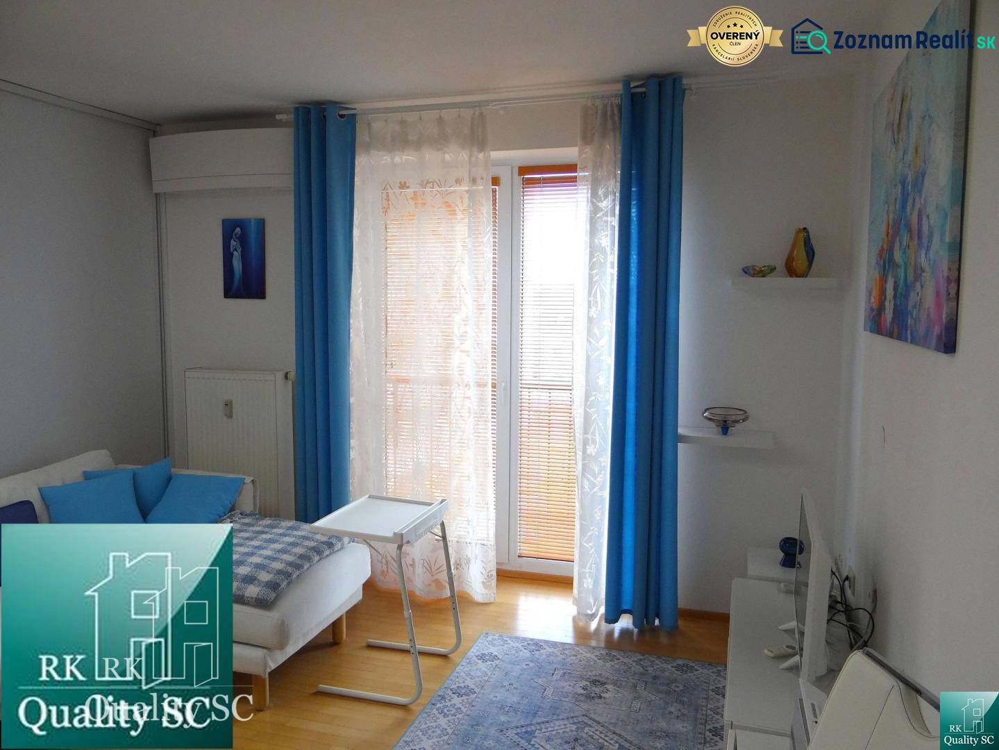 Living area of a studio apartment with blue accessories and wood-patterned flooring.