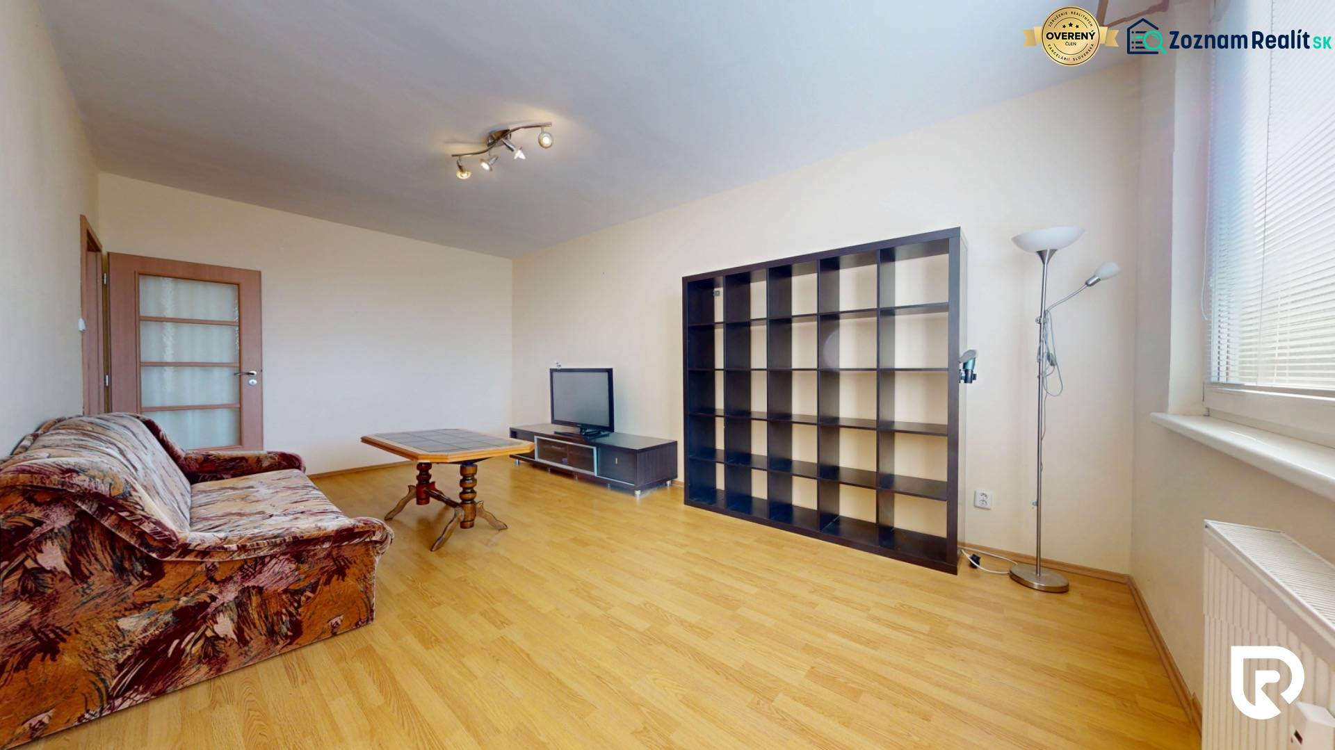 Living room in a three-room apartment with a wooden decor floor, a sofa, and a bookshelf.