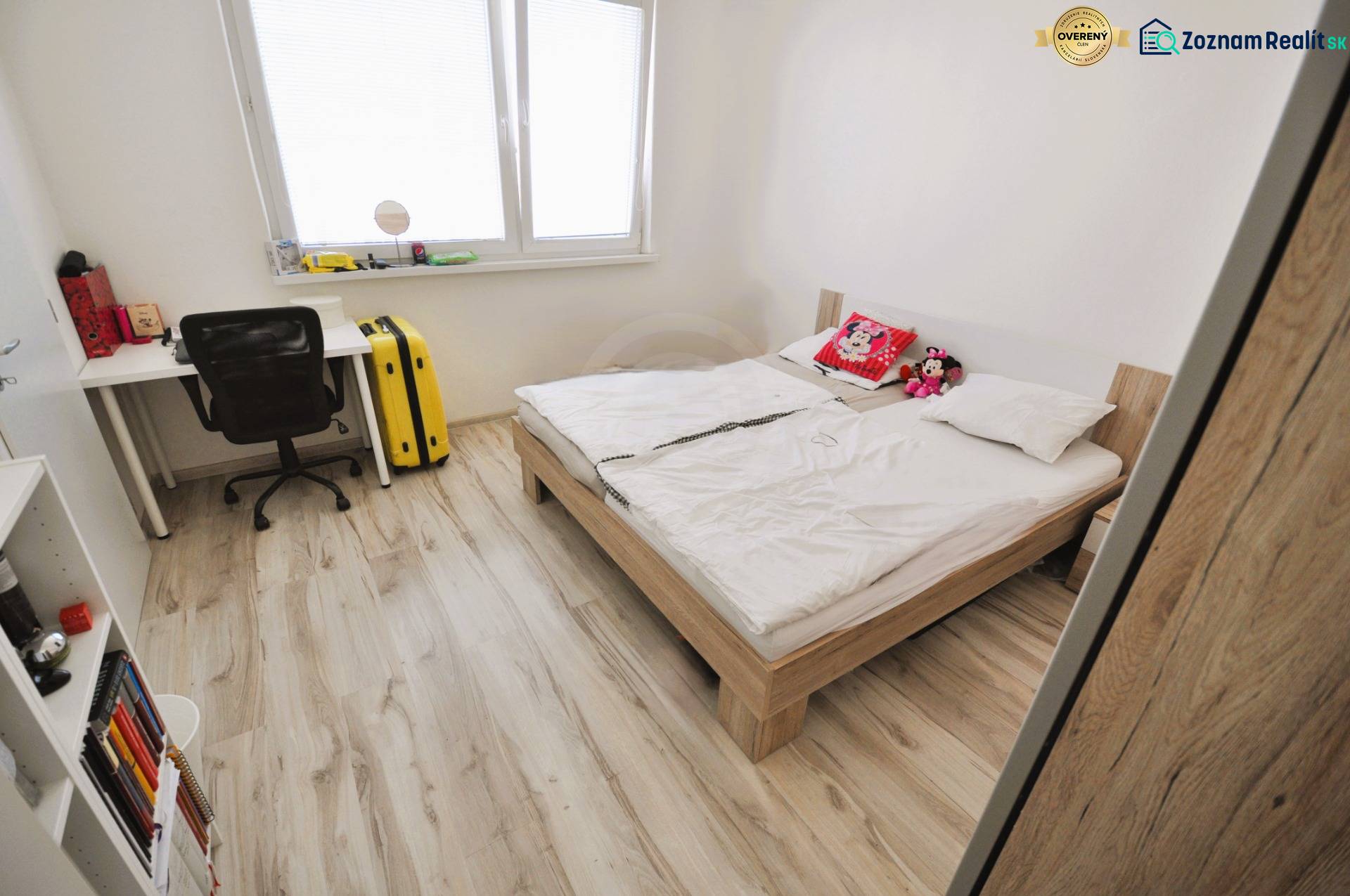 Bright bedroom in a 2-room apartment with a bed, a desk, and a floor with a wooden decor.