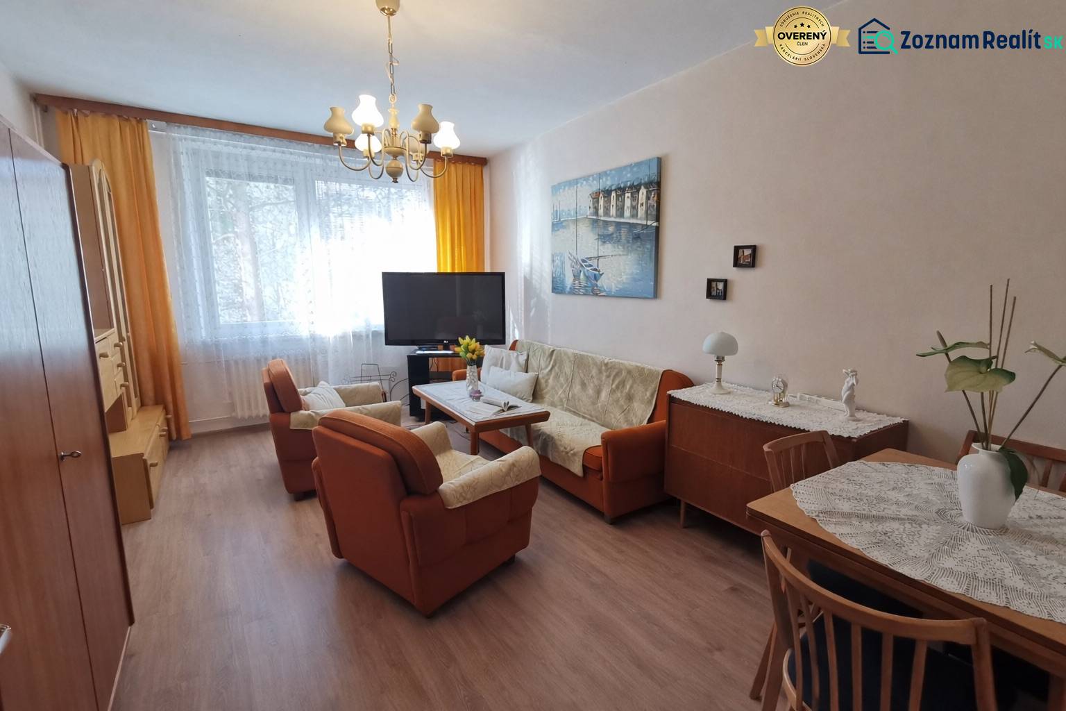 Living room in a two-room apartment with wood-decor flooring, comfortable seating, and a television.
