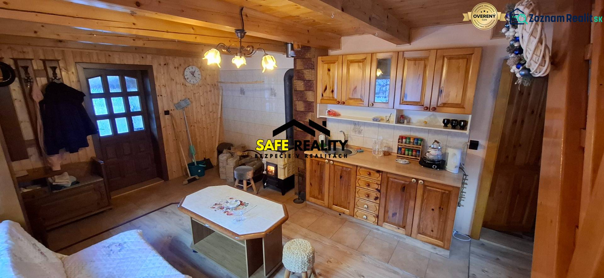 Interior of a cabin with wooden decor, kitchen unit, wood-burning stove, seating area.