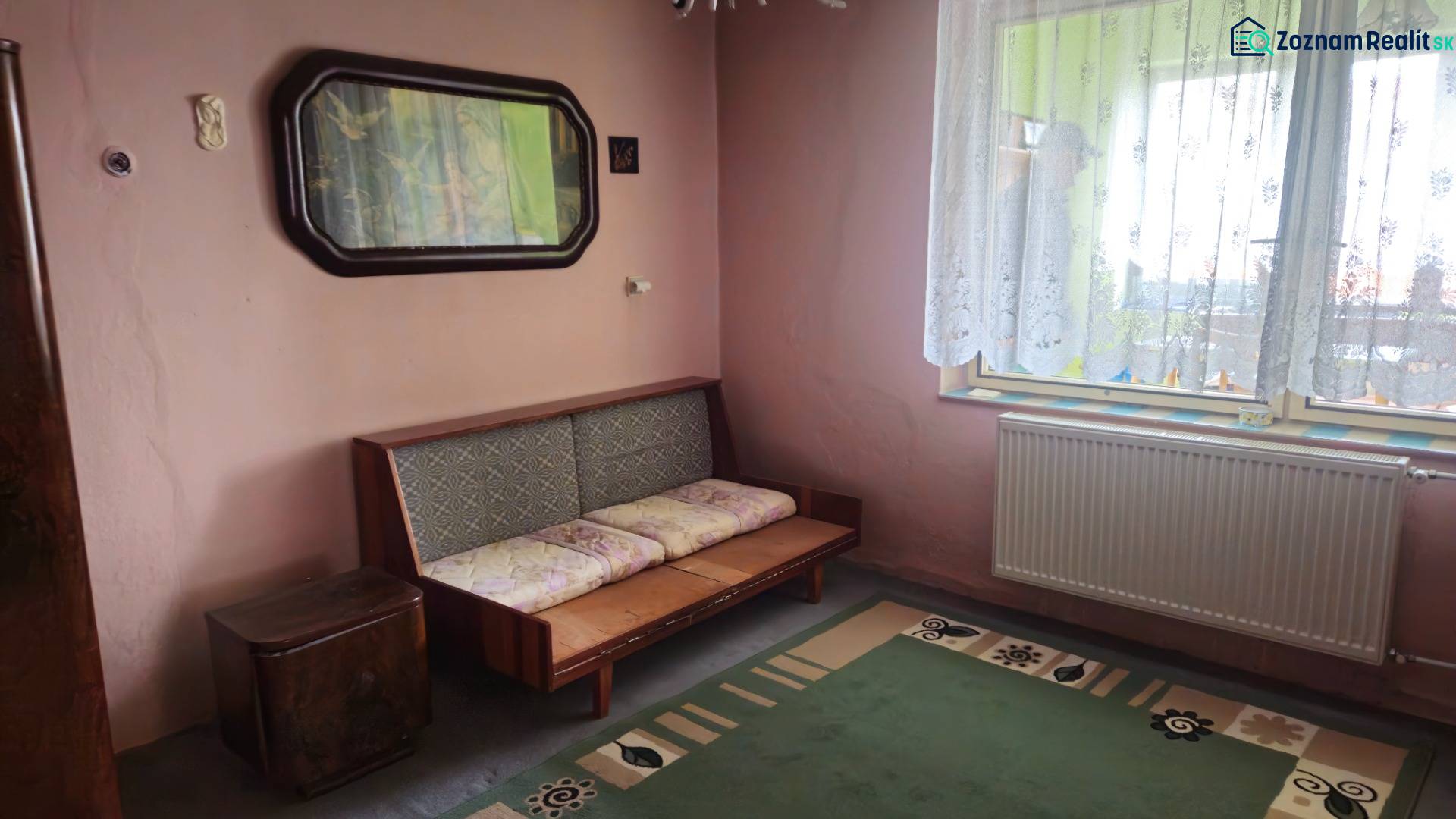 A room in a family house with a sofa, a green carpet, and an ornamental curtain.