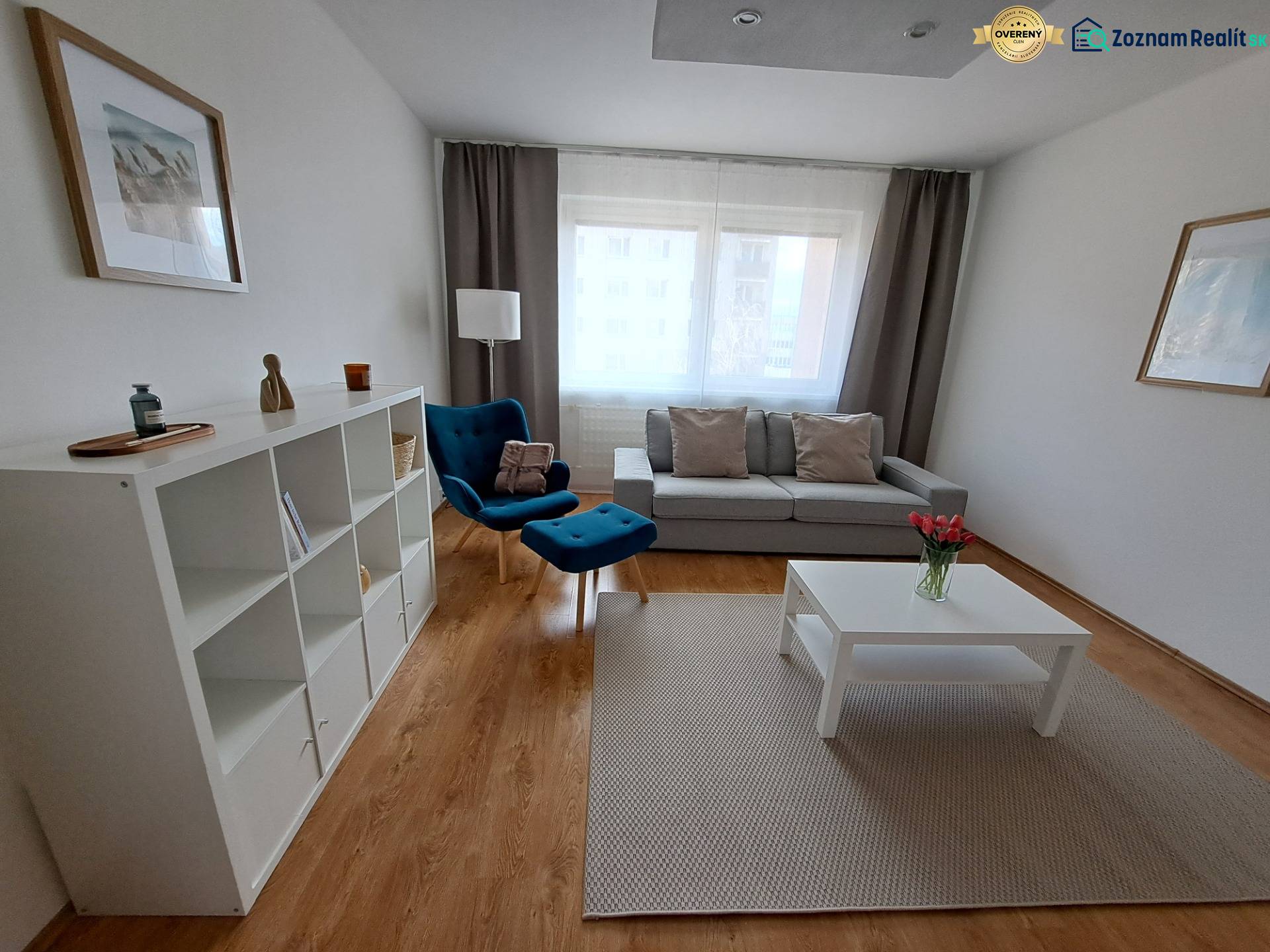 Living room in a three-room apartment with a wooden decor floor, a blue armchair, and white furniture.