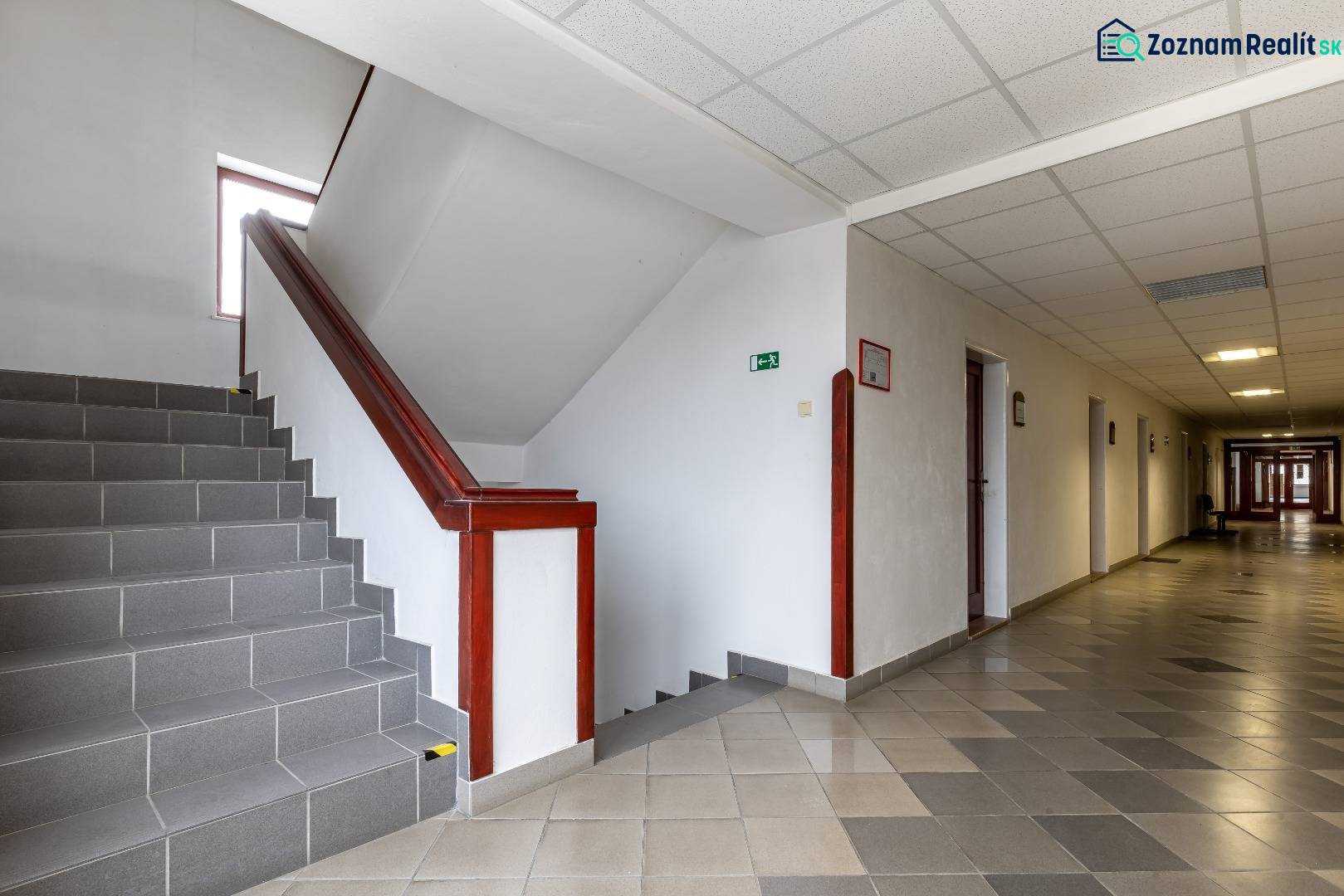 A corridor with tiles and a staircase in offices, ceiling lighting.