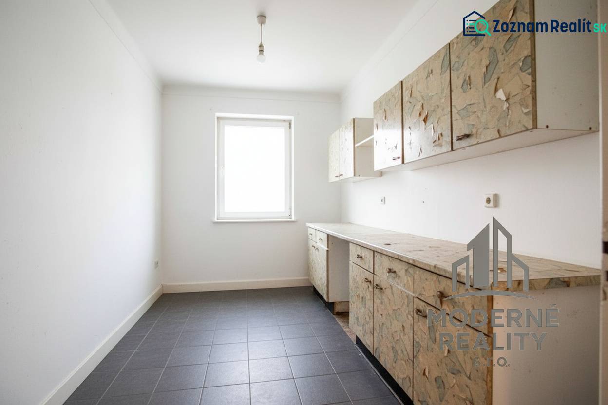 A kitchen in a family house with older cabinets and tiles on the floor.