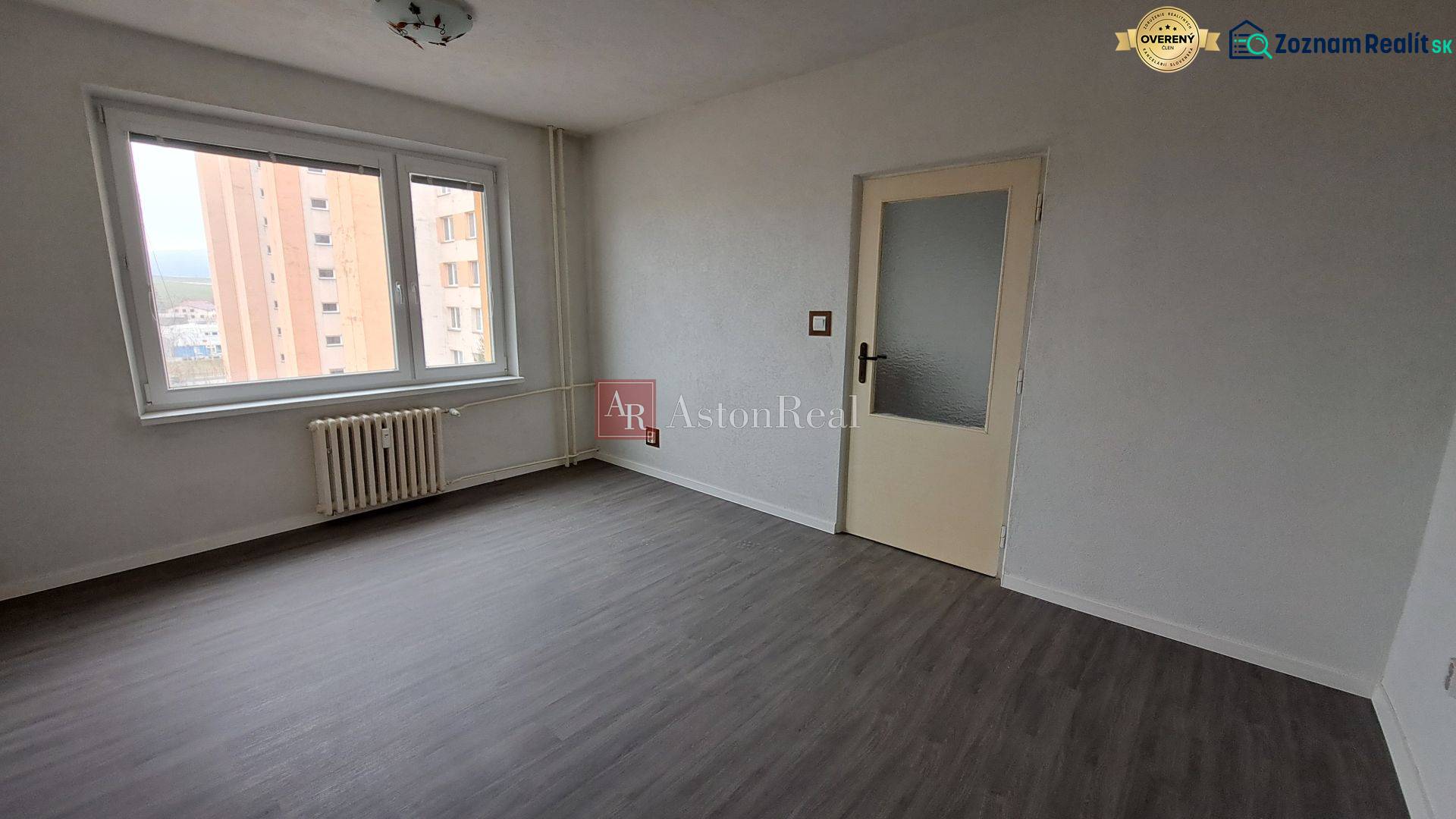 A room in a one-bedroom apartment with a large window and a floor with a wooden decor.