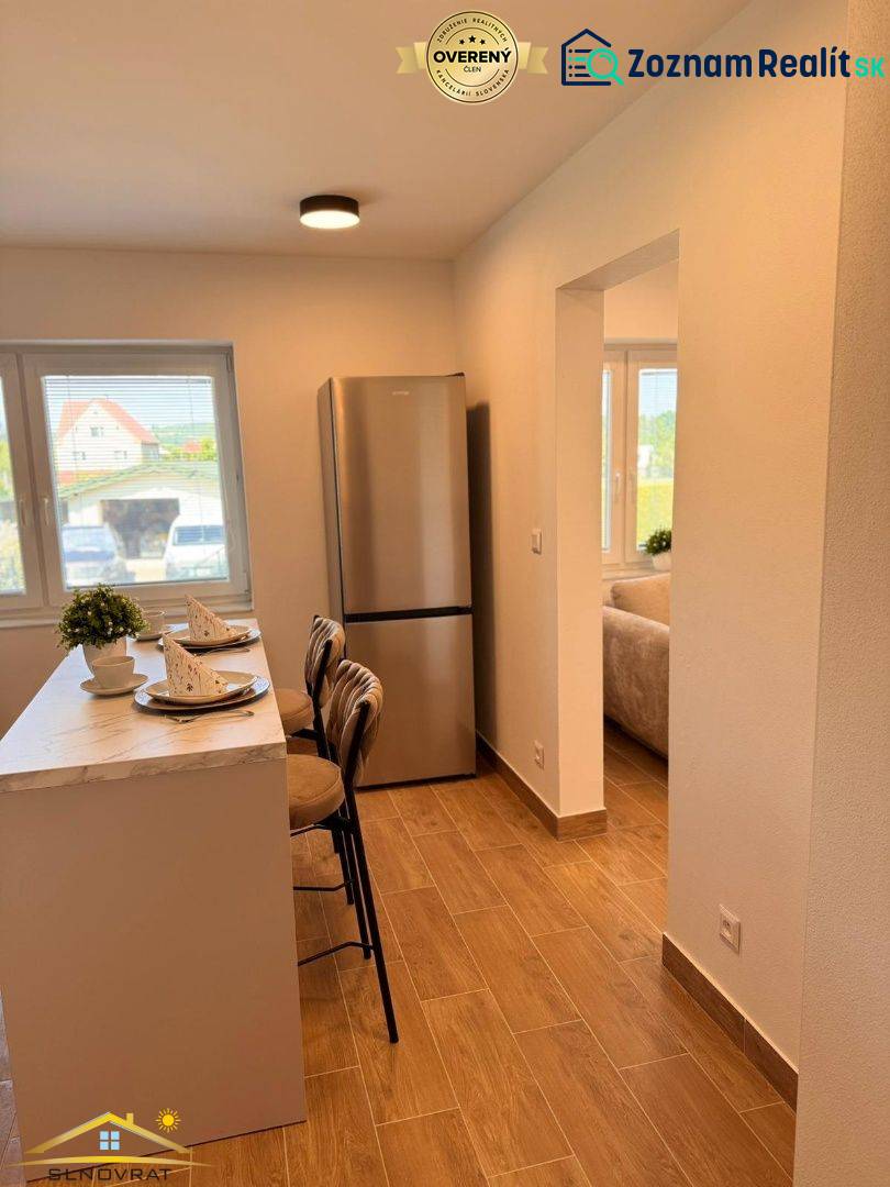 A kitchen in a 2-room apartment with a bar, wooden decor flooring, and a refrigerator.