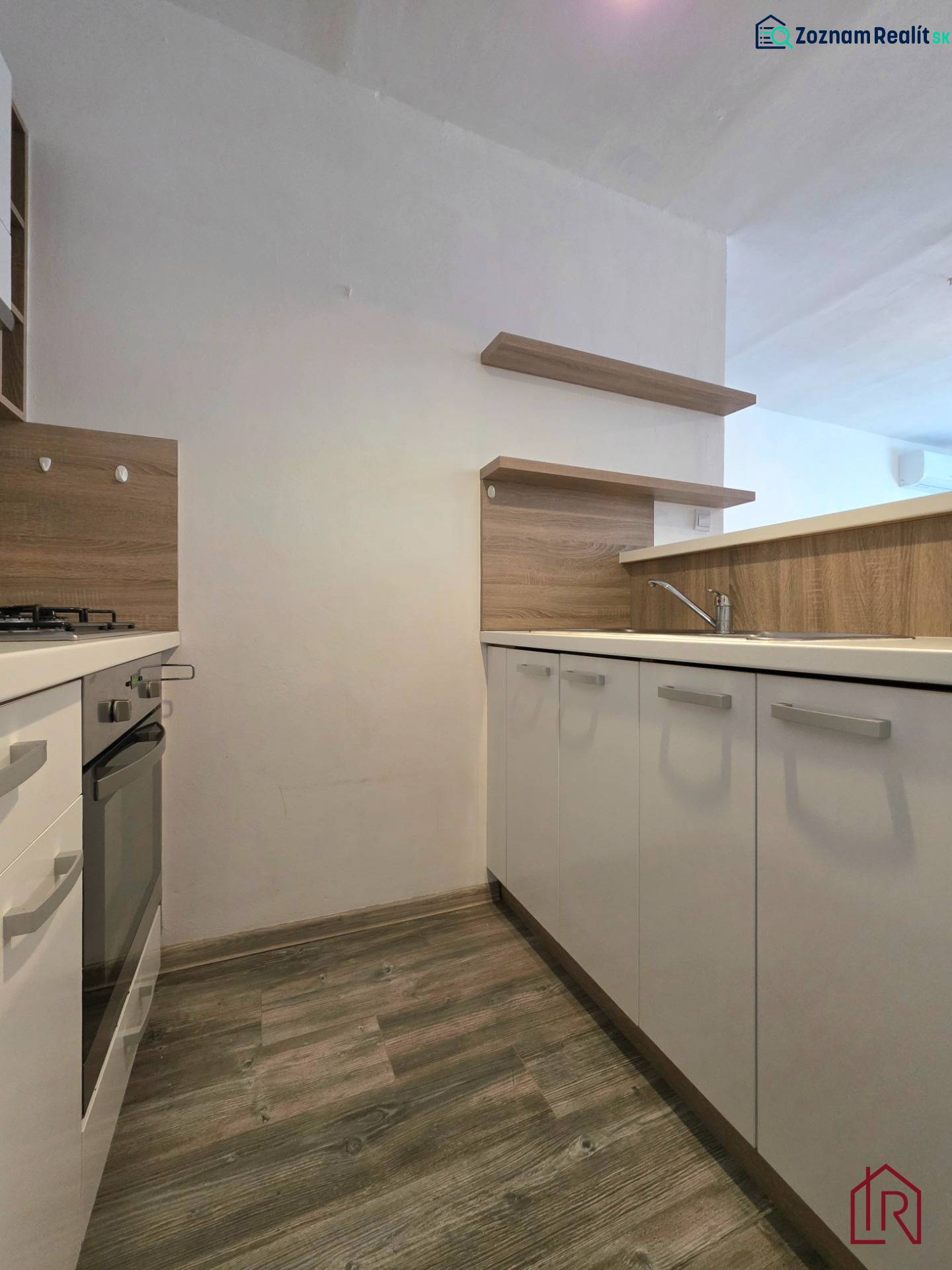 A kitchen unit in a 2-room apartment with a wood-patterned floor and a built-in oven.