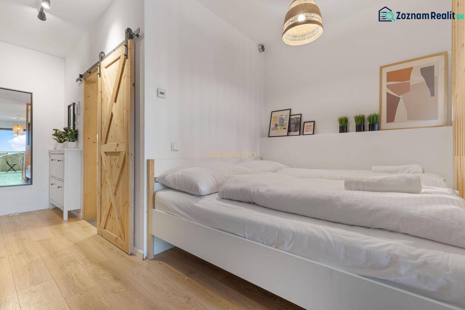 A bedroom in a studio apartment with sliding doors and a wood-patterned floor.