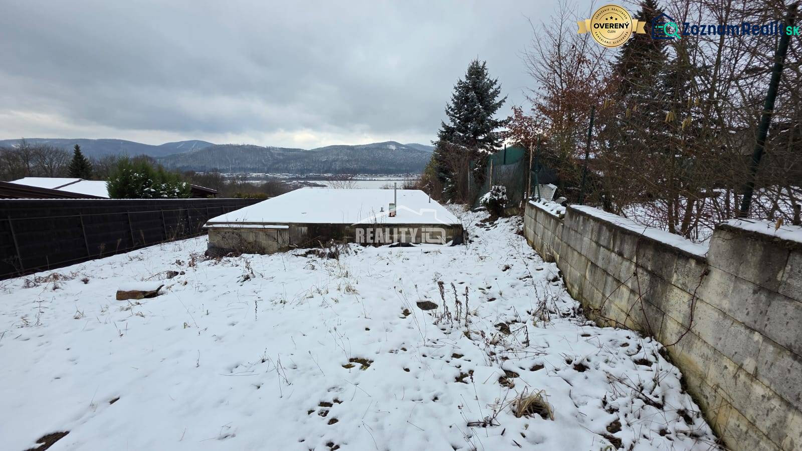 Snow-covered recreational plots in Považská Bystrica with a view of the mountains and planted trees.