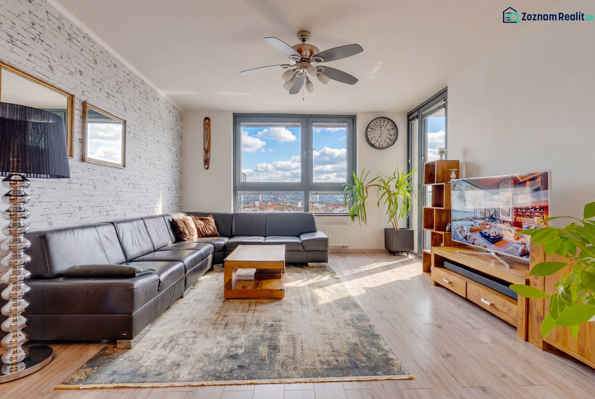 Living room in a three-room apartment with a wooden decor floor, a comfortable sofa, and large windows.