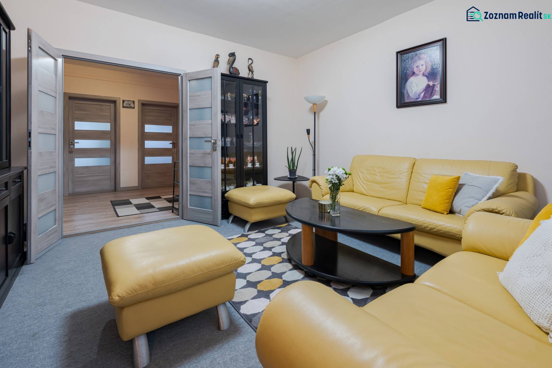 Living room of a 4-room apartment with a yellow leather sofa, glass display cabinet, and a painting on the wall.