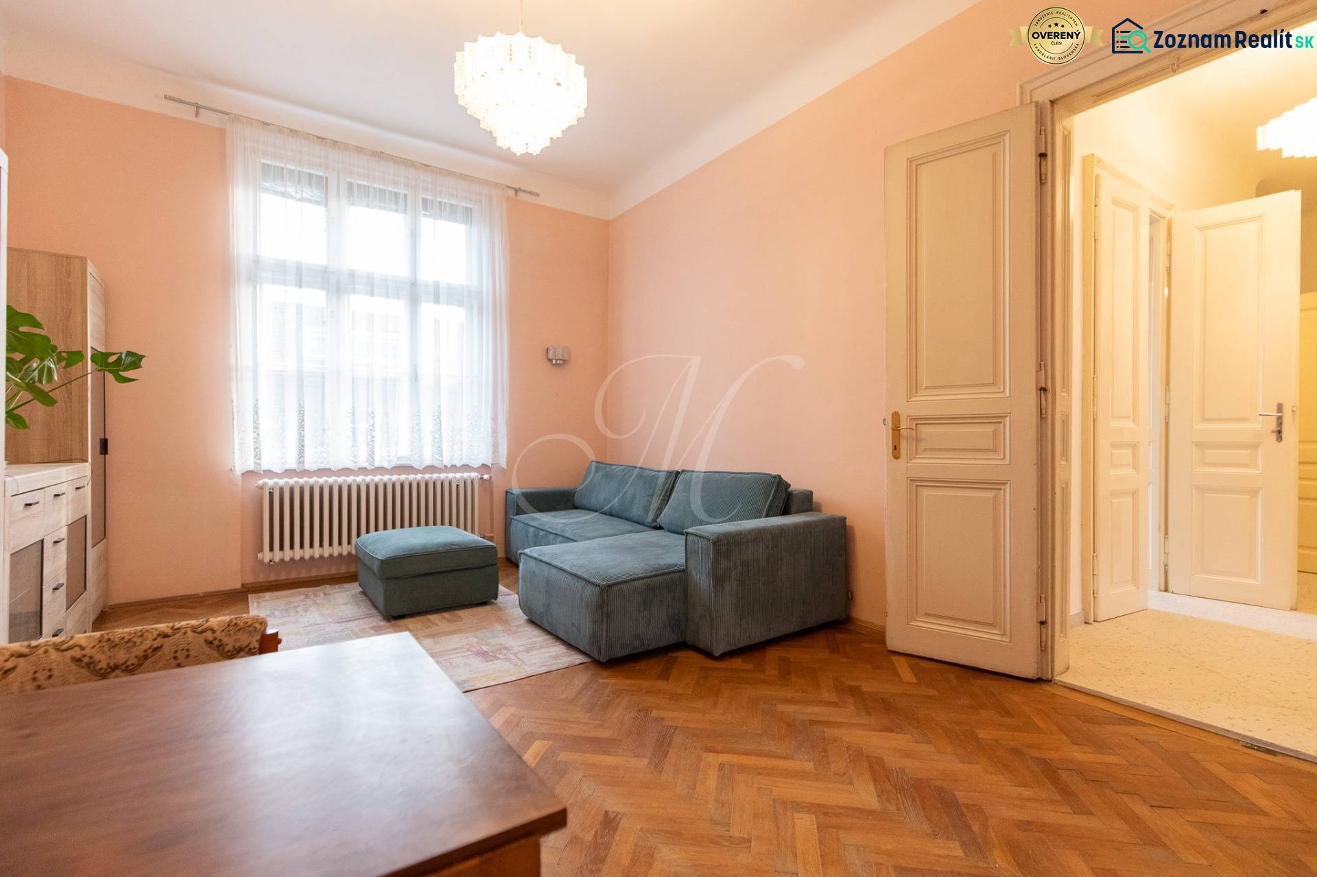 A bright living room with a sofa, chandelier, and wood-patterned flooring in a three-room apartment.
