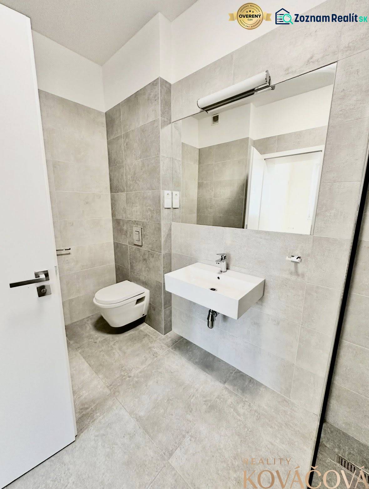 Bathroom with a sink and wall-mounted toilet, light tiles, large mirror.