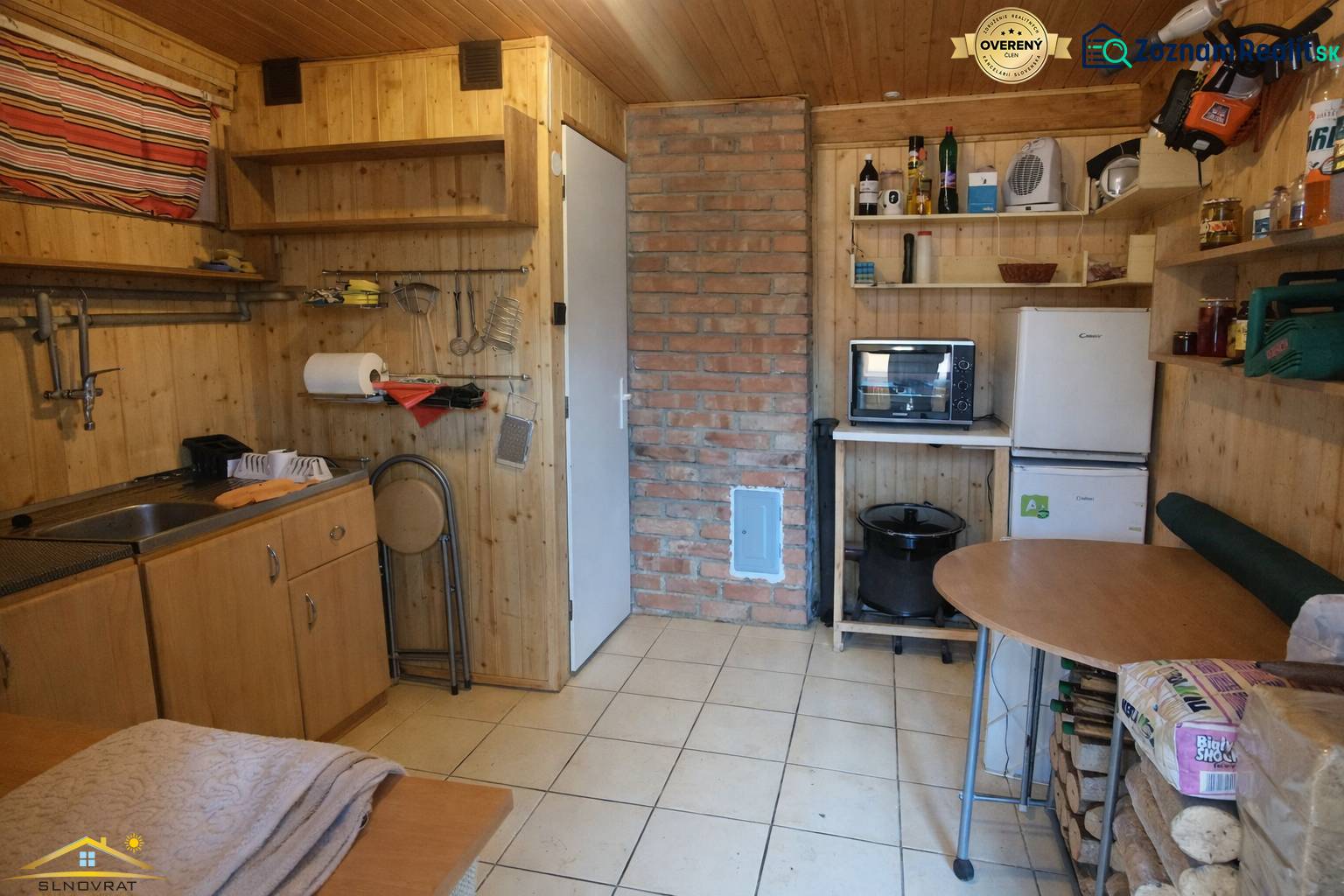 A kitchen in a cabin with wooden decor and a brick chimney, equipped with basic furniture.