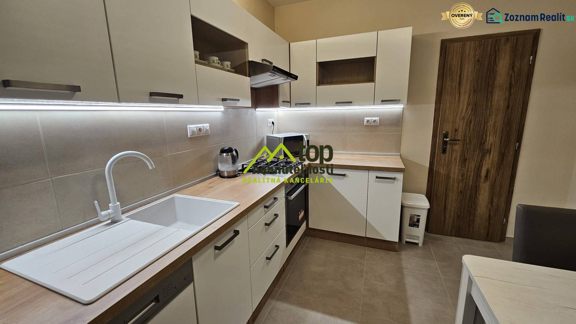 A kitchen in a 2-room apartment with white cabinets and a wooden decor floor.