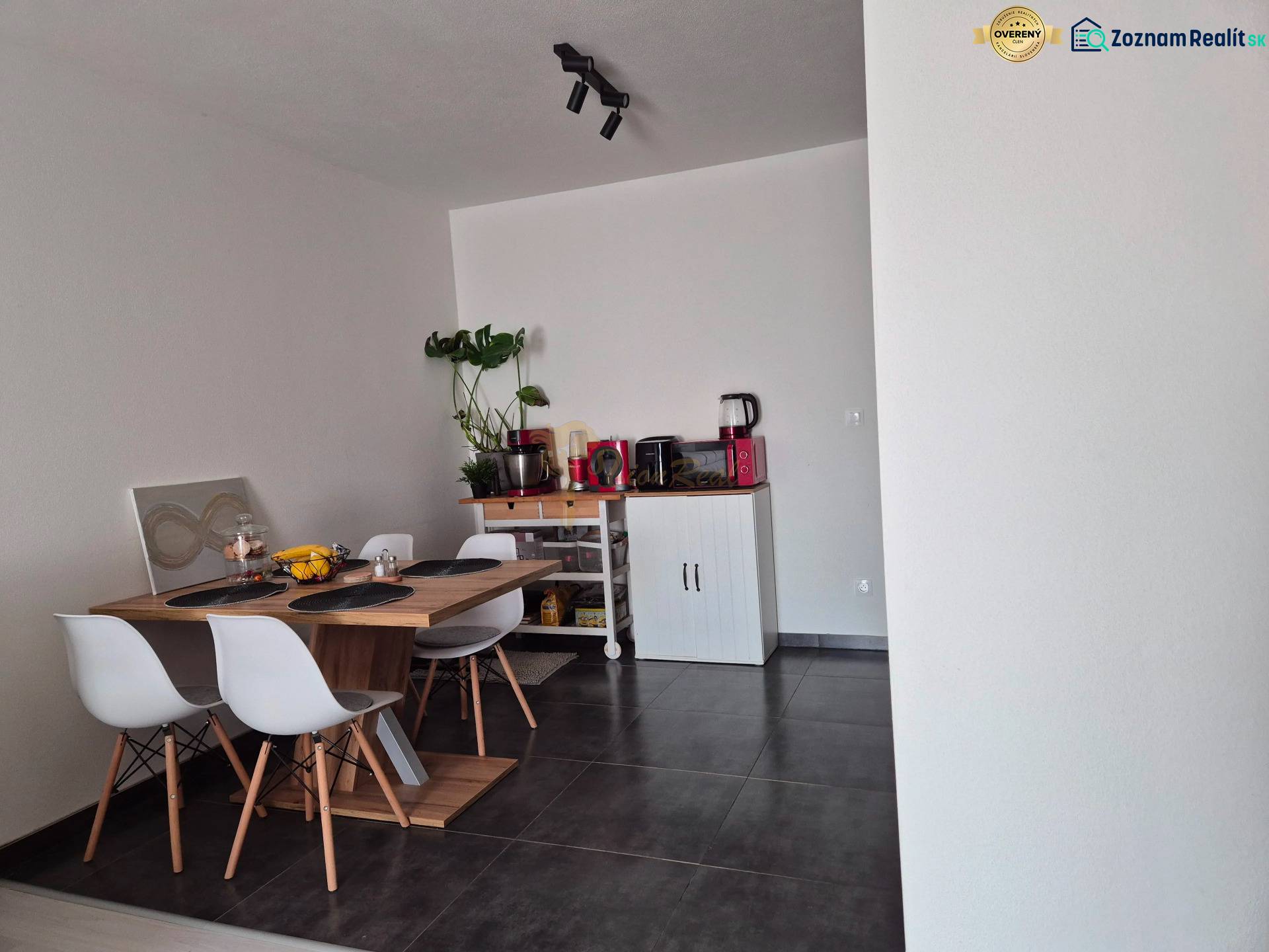 Dining area with a wooden table, four chairs, and a plant in a three-room apartment.