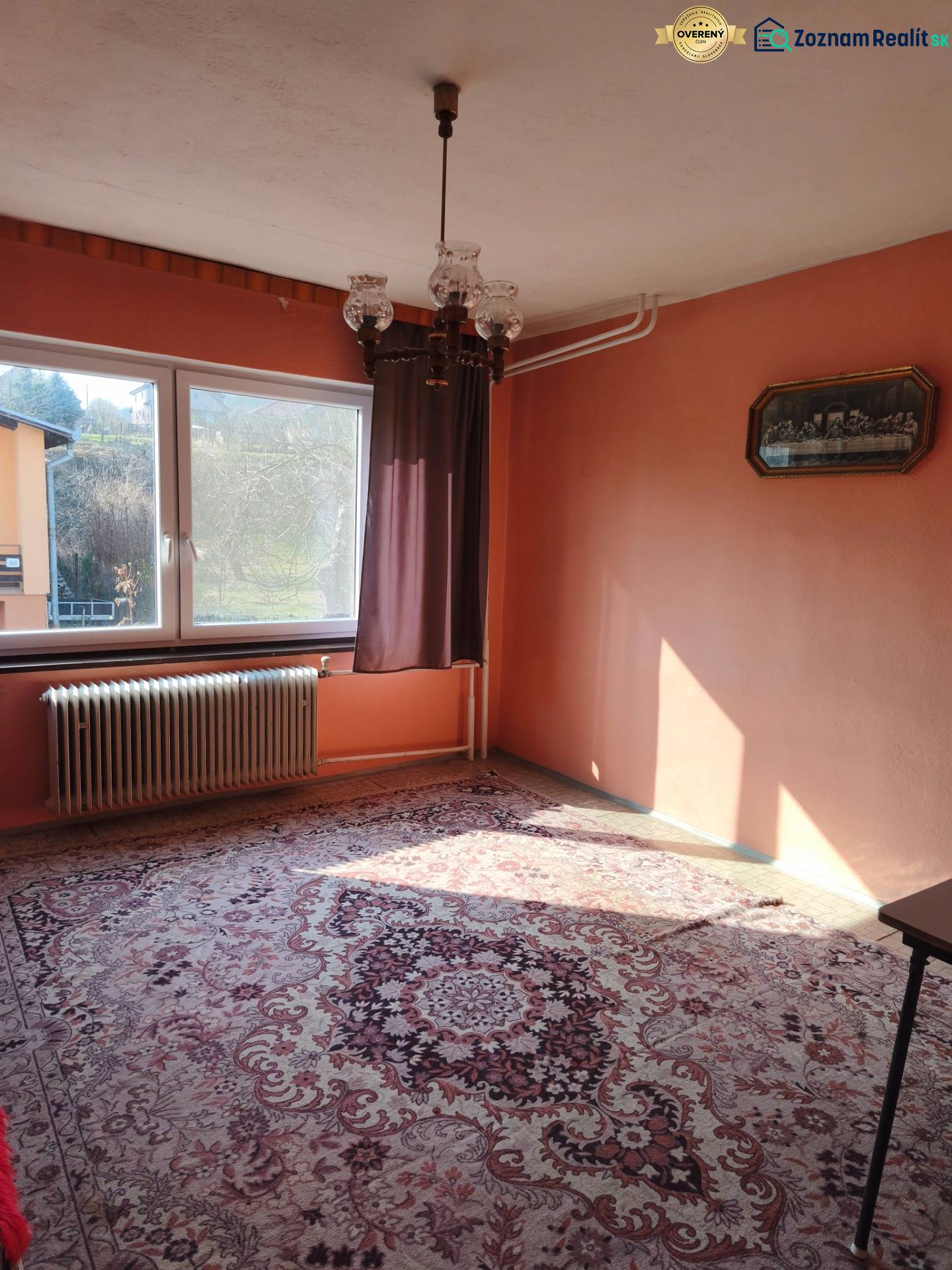 A room in a family house with a carpet, chandelier, window, and radiator, warm-colored walls.