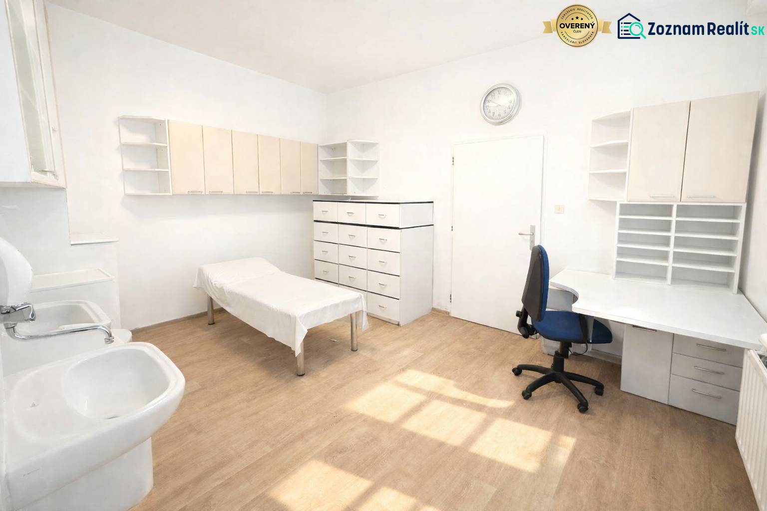 A white office with a sink and wood-patterned flooring, furnished with a desk and cabinets.